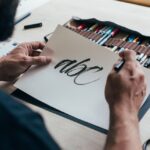 a bearded male designer holding a paper sheet with a hand-lettering saying “abc”